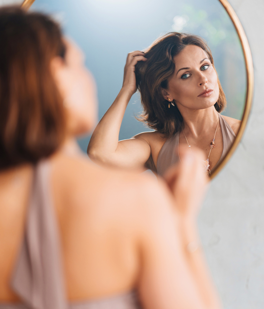 Female model looking in a mirror and adjusting hair, MOHS Reconstruction Surgery in NYC